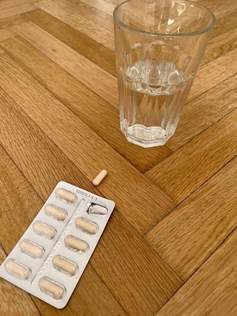 Probiotikus kapsle se skleničkou vody na dřevěných parketách